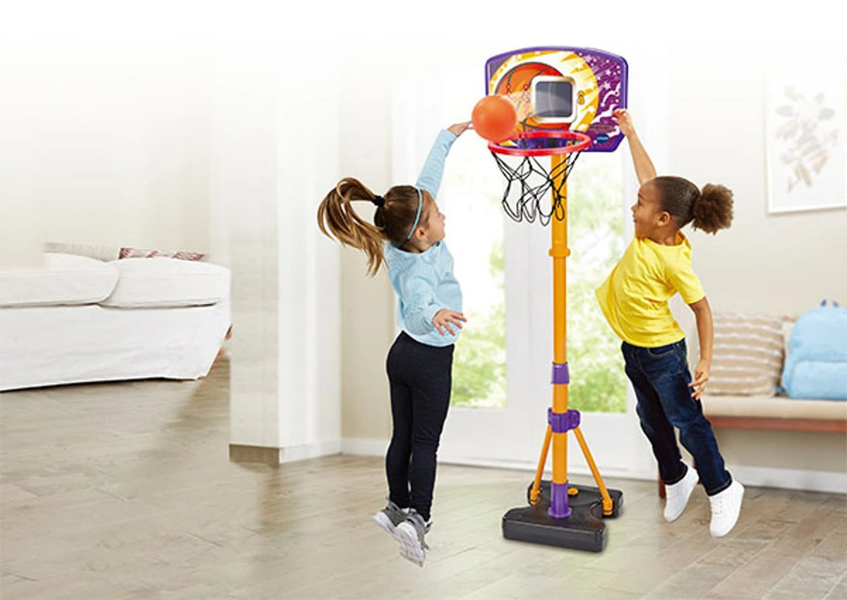 Two children reaching for the orange basketball at the VTech Counting Hoops Basketball Stand with electronic backboard and net