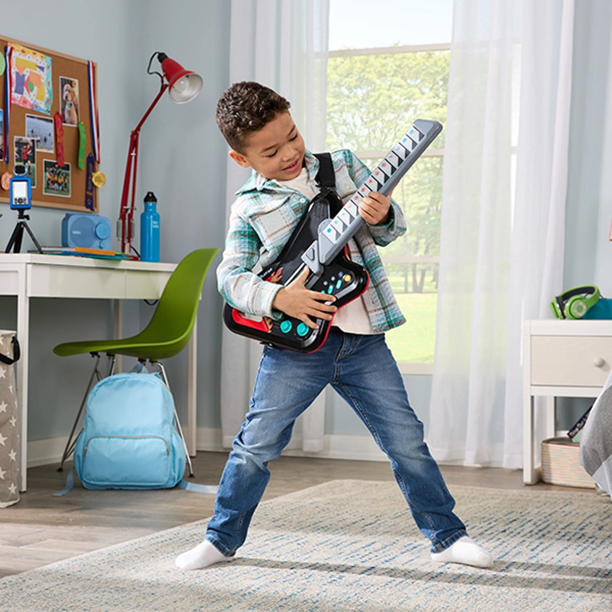 Child standing and playing the VTech Kidi Guitar Superstar with the black shoulder strap fitted