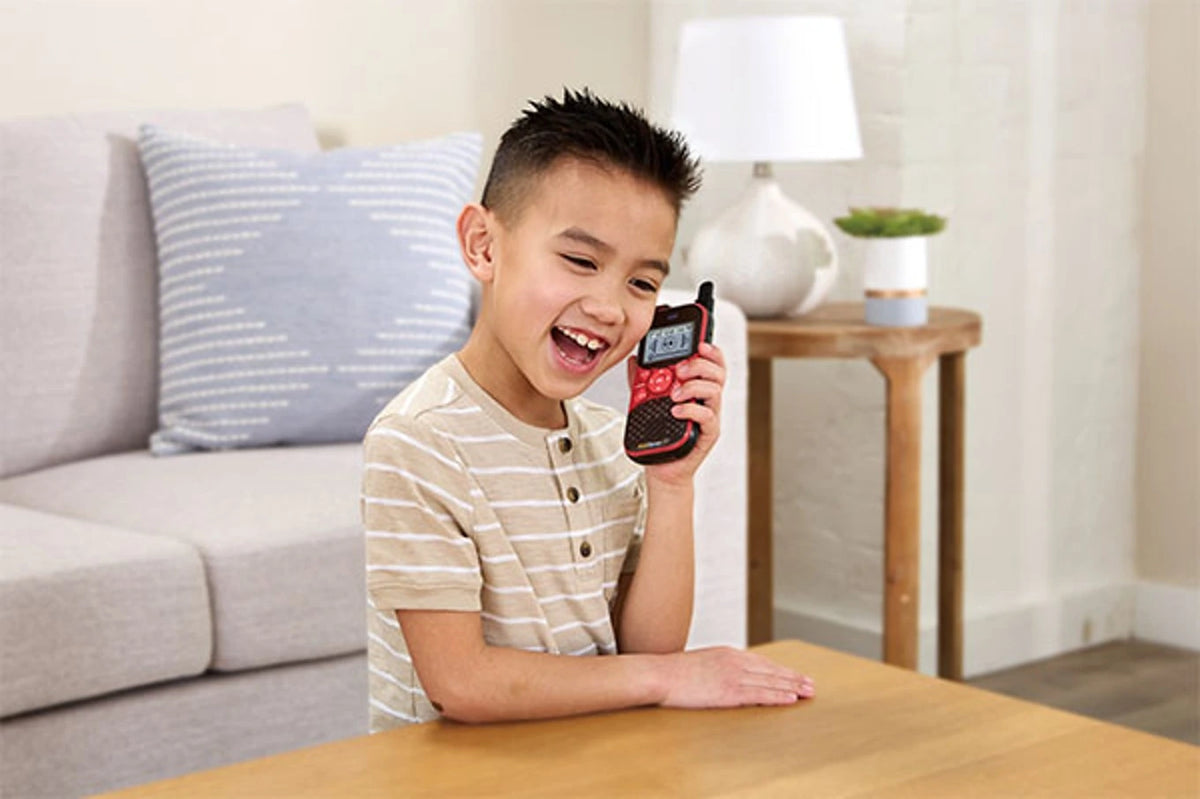 Child speaking into the red VTech KidiGear Walkie Talkies Explorer beside a table