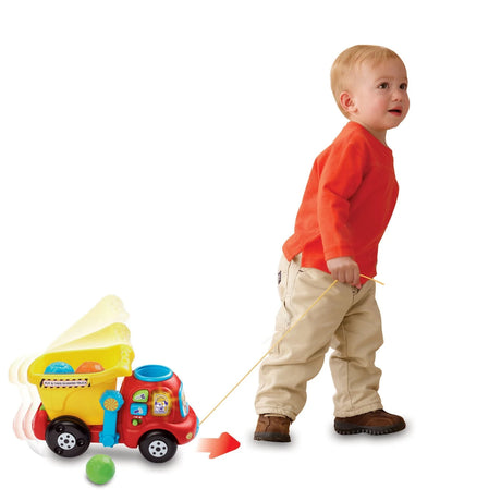 Toddler holding the pull cord beside the VTech Put & Take Dumper Truck with green rock on the floor