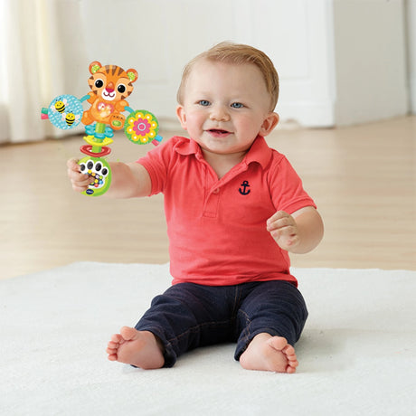 Baby seated on light coloured mat holding VTech Rattle & Roar Tiger rattle upright in right hand