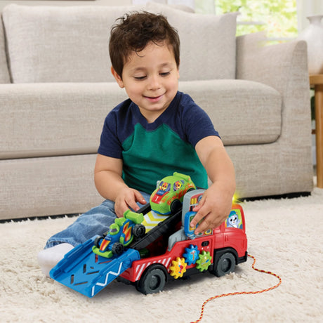 Child sitting on carpet playing with VTech Road Rescue Car Carrier with ramp lowered and green and blue sports cars loaded