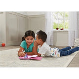 Two children lying on a rug with the VTech Secret Safe Magic Notebook open, one writing while the other whispers in her ear