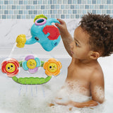 Child sitting in bath pouring water from blue elephant watering can onto spinning flower attachment fixed to bath wall