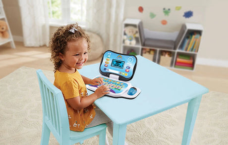 Child sitting at a blue table with VTech Toddler Tech Laptop open