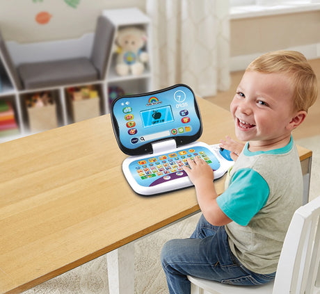 Child sitting at a wooden table with VTech Toddler Tech Laptop open