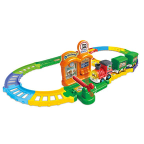 Assembled Chug & Learn Train Set track with colourful oval layout, orange station piece, green and yellow track segments, red train engine with two green wagons, and station gate lever.