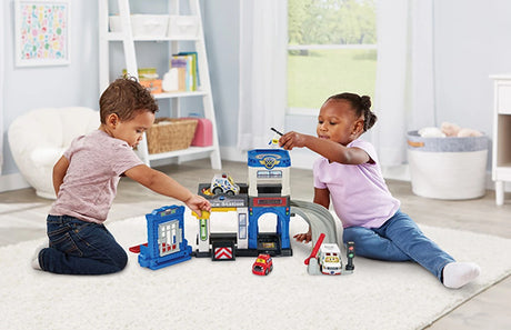 Two children playing with VTech Toot-Toot Drivers Police Station playset on a floor 