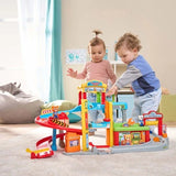 Two children standing beside the VTech Toot-Toot Drivers Roll & Repair Garage while playing with the track