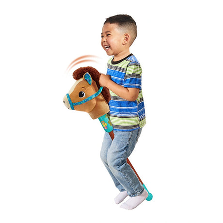 Child riding VTech Trotting Tunes Hobby Horse holding plush horse head with motion lines above mane and turquoise base cap on stick