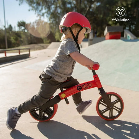 Child wearing a red helmet riding Yvolution Velo Junior Balance Bike Red