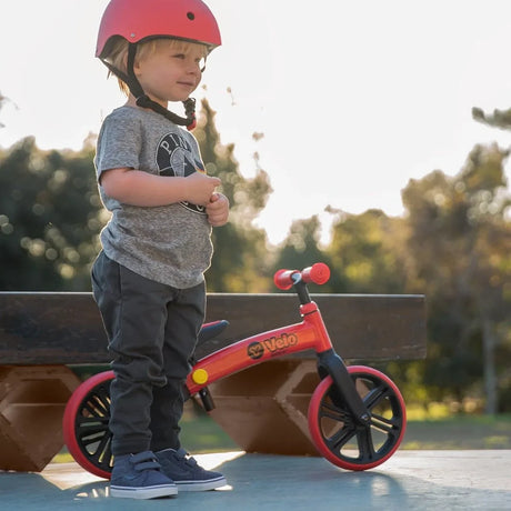 Child wearing a red helmet standing beside Yvolution Velo Junior Balance Bike Red
